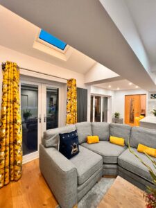 Open plan kitchen-living space with corner sofa and Velux skylight.